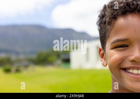 Un garçon biracial aux cheveux bouclés sourit dehors, copie l'espace Banque D'Images