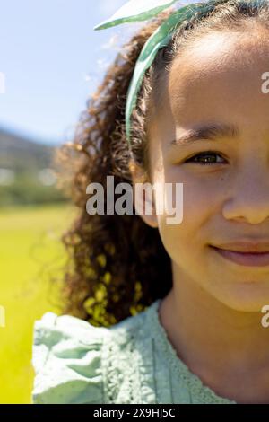 Fille biraciale avec des cheveux bouclés souriant dans un cadre extérieur ensoleillé Banque D'Images