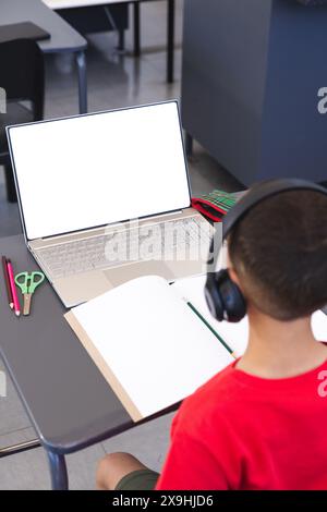 Garçon biracial étudiant à l'école à l'aide d'un ordinateur portable, avec espace de copie Banque D'Images