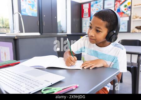 Garçon biracial étudie attentivement à l'école en utilisant un ordinateur portable Banque D'Images