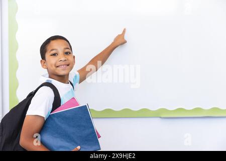 Biracial Boy pointe vers un tableau blanc dans une salle de classe à l'école Banque D'Images