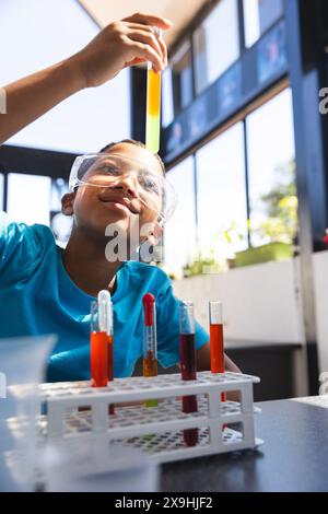 Biracial Boy examine un tube à essai dans une salle de classe de laboratoire d'école Banque D'Images