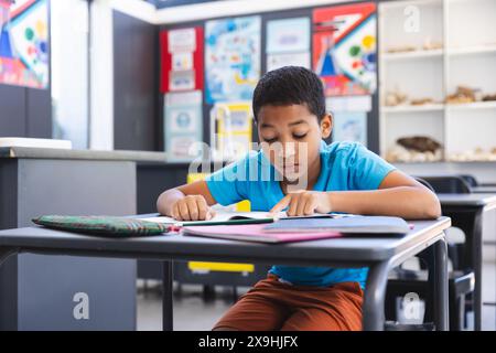 Garçon biracial concentré sur le travail scolaire dans une salle de classe à l'école Banque D'Images