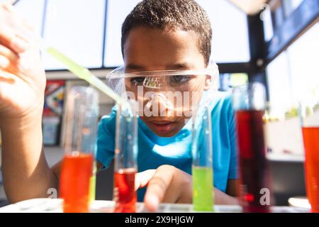 Biracial Boy examine des éprouvettes dans un laboratoire scolaire Banque D'Images