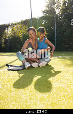 À l'extérieur, mère biraciale et fille sourire sur un court de tennis tenant des raquettes de tennis Banque D'Images