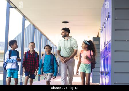 À l'école, un enseignant asiatique marche avec quatre élèves biraciaux Banque D'Images