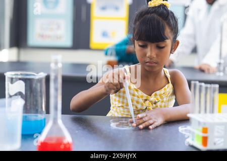 Fille biraciale dans une robe jaune mène une expérience scientifique à l'école. Elle se concentre sur le placement d'une substance sur une boîte de Pétri dans un laboratoire Banque D'Images