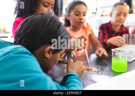 Les enfants biraciaux se livrent à une expérience scientifique à l'école, l'un observant à travers une loupe. Ils sont concentrés et curieux, explorant la chimie Banque D'Images