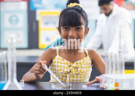 Une fille biraciale en robe jaune tient une pipette, souriante Banque D'Images