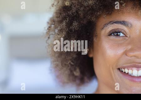 À la maison, jeune femme biraciale montrant des cheveux bouclés et des yeux bruns, rayonnant de joie, copiez l'espace Banque D'Images