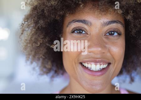 À la maison, jeune femme biraciale portant un haut rose, montrant une expression joyeuse Banque D'Images