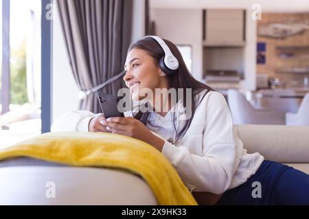 Une jeune femme biraciale portant des écouteurs, se relaxant à la maison Banque D'Images