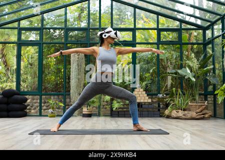 Pacific Islander femme dans le casque VR pratique le yoga au Glass House Studio Banque D'Images