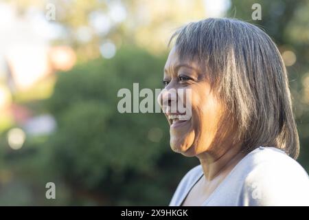 À l'extérieur, femme biraciale senior souriant dans un jardin luxuriant avec des arbres, espace de copie Banque D'Images