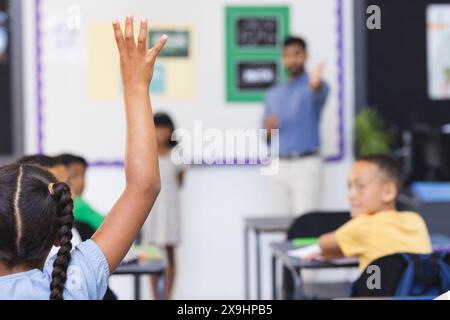 À l'école, un jeune enseignant asiatique se tient près d'un conseil dans la salle de classe, les élèves levant la main Banque D'Images