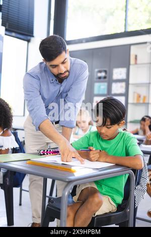 Un jeune enseignant asiatique assiste un garçon biracial dans une salle de classe Banque D'Images