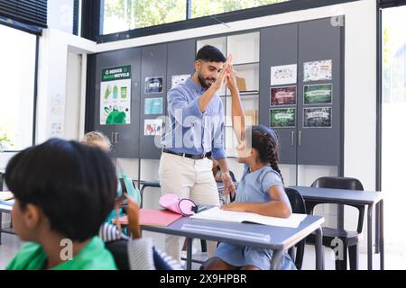 Jeune professeur asiatique de sexe masculin de haut-cinq ans une fille biraciale dans une classe d'école Banque D'Images