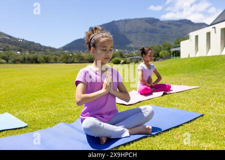 Deux filles biraciales pratiquent le yoga en plein air par une journée ensoleillée Banque D'Images