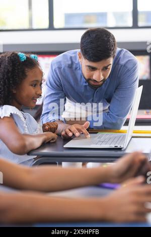 À l'école, enseignant asiatique montrant un ordinateur portable à une étudiante biraciale en classe Banque D'Images