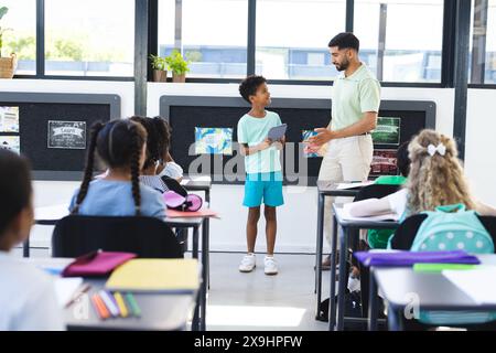 À l'école, un jeune enseignant asiatique parle à un étudiant biracial Banque D'Images