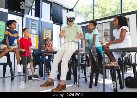 À l'école, un enseignant asiatique portant un casque VR se tient devant de jeunes élèves. Quatre étudiants biraciaux regardent, fascinés par la démonstration de technologie, u Banque D'Images