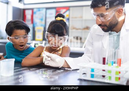 Des enfants biraciaux participent à une expérience scientifique avec un jeune enseignant asiatique à l'école Banque D'Images