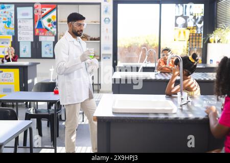 À l'école, un enseignant asiatique tenant un bécher se tient près de divers jeunes élèves qui font des expériences scientifiques. Ils portent des vêtements décontractés, entourés de che Banque D'Images