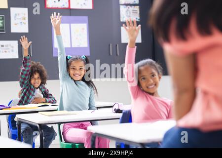 À l'école, une jeune femme biraciale enseigne à trois jeunes élèves en classe Banque D'Images