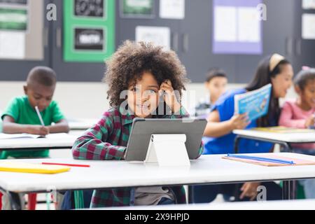 Jeune fille biraciale avec des cheveux bouclés en utilisant la tablette en classe Banque D'Images