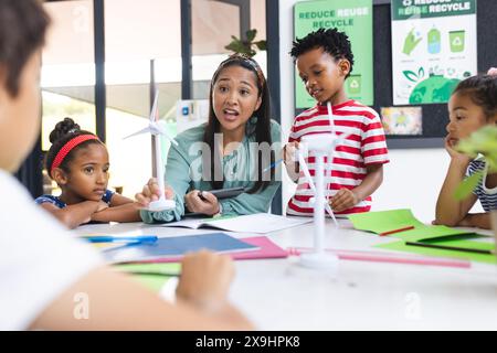 Un enseignant biracial d'âge moyen et quatre jeunes élèves travaillent ensemble dans une salle de classe Banque D'Images