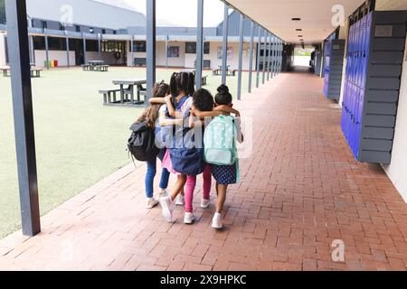 À l'école, quatre jeunes filles biraciales marchent ensemble à l'extérieur Banque D'Images