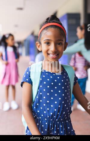 Jeune fille biraciale portant une robe à pois et un sac à dos souriant à l'extérieur Banque D'Images