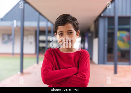 À l'école, jeune étudiant biracial debout, les bras croisés à l'extérieur Banque D'Images