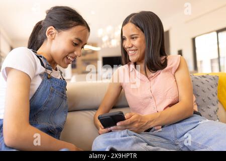 Jeunes sœurs biraciales à la maison, regardant un smartphone Banque D'Images