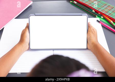 Fille biraciale dans la classe tient la tablette avec écran blanc pour l'espace de copie Banque D'Images