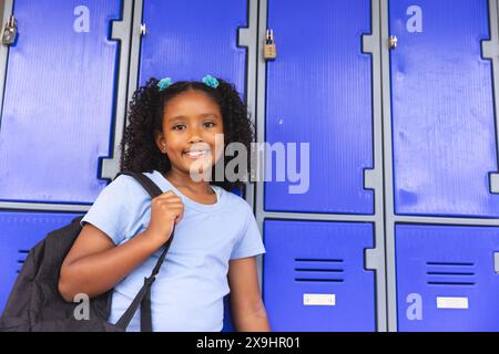 Fille biraciale se tient près des casiers de l'école, avec espace de copie Banque D'Images