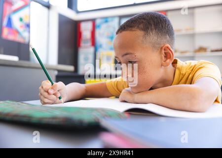 Biracial Boy se concentre sur le travail scolaire à l'école Banque D'Images