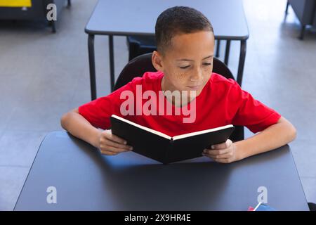 Un garçon biracial lit un livre à l'école Banque D'Images