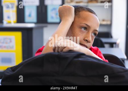 Biracial Boy a l'air réfléchi dans une salle de classe à l'école Banque D'Images