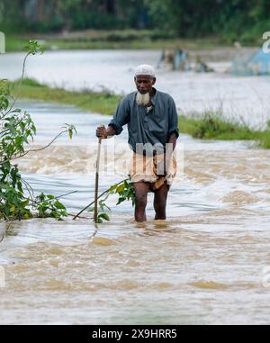 Sylhet, Bangladesh. 30 mai 2024. Les résidents âgés ont du mal à patauger sur la route principale inondée dans le quartier Lafnaut de Gowainghat upazila de Sylhet. Les pluies continues du cyclone Remal ont provoqué l'écoulement de l'eau des collines environnantes, submergeant la route depuis hier. Il est à noter que de nombreuses personnes ont quitté leur domicile et se sont rendues dans des refuges sûrs. Les zones basses et horifères de trois syndicats de l'upazila de Jaintapur à Sylhet sont inondées en raison de crues soudaines provoquées par de fortes pluies et de l'eau des pentes des collines. Environ 300 mille personnes dans quatre upazilas ont été piégées dans l'eau due Banque D'Images