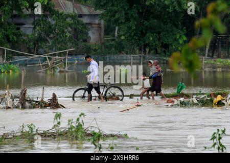 Sylhet, Bangladesh. 30 mai 2024. Les habitants de l'upazila Gowainghat de Sylhet traversent une route principale inondée dans la région de Lafnaut, submergée depuis hier alors que la pluie continue des suites du cyclone Remal envoie de l'eau jaillir des collines environnantes. Il est à noter que de nombreuses personnes ont quitté leur domicile et se sont rendues dans des refuges sûrs. Les zones basses et horifères de trois syndicats de l'upazila de Jaintapur à Sylhet sont inondées en raison de crues soudaines provoquées par de fortes pluies et de l'eau des pentes des collines. Environ 300 000 personnes dans quatre upazilas ont été piégées dans l'eau en raison des inondations soudaines. Banque D'Images