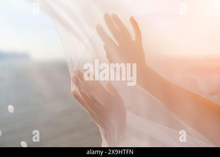 Les mains d'une femme sont montrées dans un voile blanc, avec le soleil qui brille dessus. Concept de paix et de sérénité, car les mains de la femme sont ouvertes et détendues. Banque D'Images