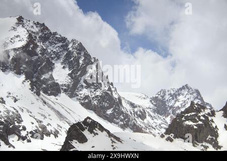 Roches acérées recouvertes de neige de sommets montagneux sur fond de ciel avec des nuages Banque D'Images
