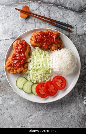 Ayam geprek un poulet frit indonésien à la sauce sambal servi avec du riz blanc, du concombre, de la tomate et du chou en gros plan sur l'assiette sur la table. Vert Banque D'Images