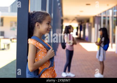 Fille biraciale avec une robe à pois se tient près d'un pilier à l'école, souriante, avec un espace de copie Banque D'Images