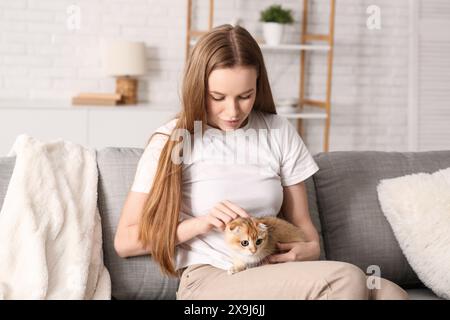 Jeune femme caressant chaton mignon sur le canapé à la maison Banque D'Images