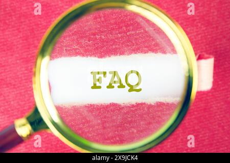 FAQ concept à travers une loupe sous un morceau de papier rouge déchiré Banque D'Images
