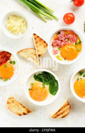 Oeufs en cocotte (oeufs cuits au four) en ramequins et toasts sur fond clair. Plat pour le petit déjeuner ou le déjeuner sain. Vue de dessus, pose à plat Banque D'Images