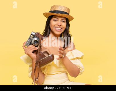 une femme robe inyellow et chapeau prenant des photos par appareil photo vintage sur un fond jaune. Des gens heureux qui partent en vacances, vacances Banque D'Images