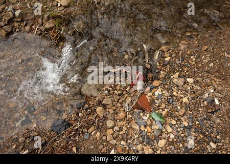 Un petit courant naturel d'eau avec des morceaux et des morceaux de déchets mélangés avec les roches le long du bord de celui-ci. Banque D'Images